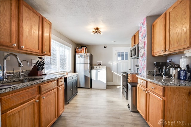 kitchen featuring appliances with stainless steel finishes, washer / dryer, sink, dark stone counters, and light wood-type flooring