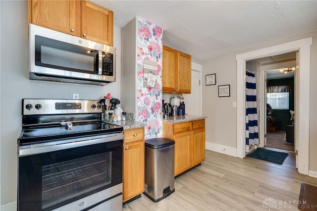 kitchen with appliances with stainless steel finishes, light stone countertops, a textured ceiling, and light hardwood / wood-style flooring