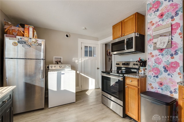 kitchen with washer / clothes dryer, light hardwood / wood-style flooring, light stone countertops, and appliances with stainless steel finishes