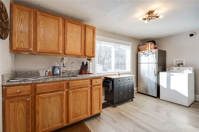 kitchen with stainless steel refrigerator, washer / clothes dryer, sink, a textured ceiling, and light wood-type flooring