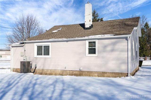 snow covered back of property featuring central AC unit