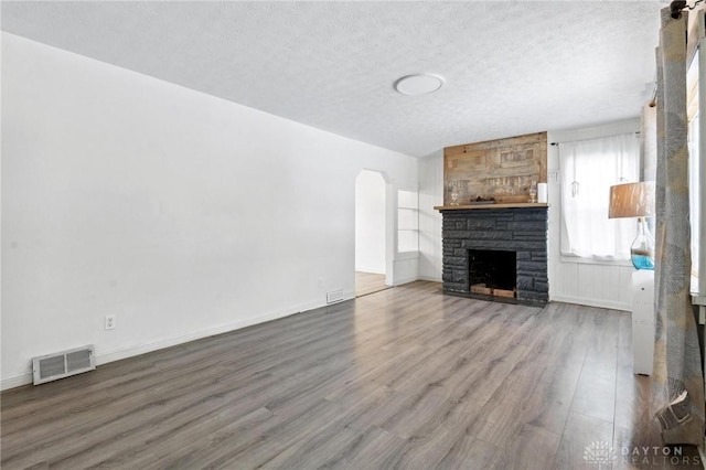 unfurnished living room featuring a textured ceiling, hardwood / wood-style floors, and a stone fireplace