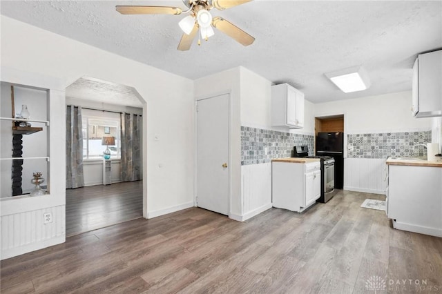 kitchen with stainless steel electric stove, white cabinetry, backsplash, light wood-type flooring, and ceiling fan