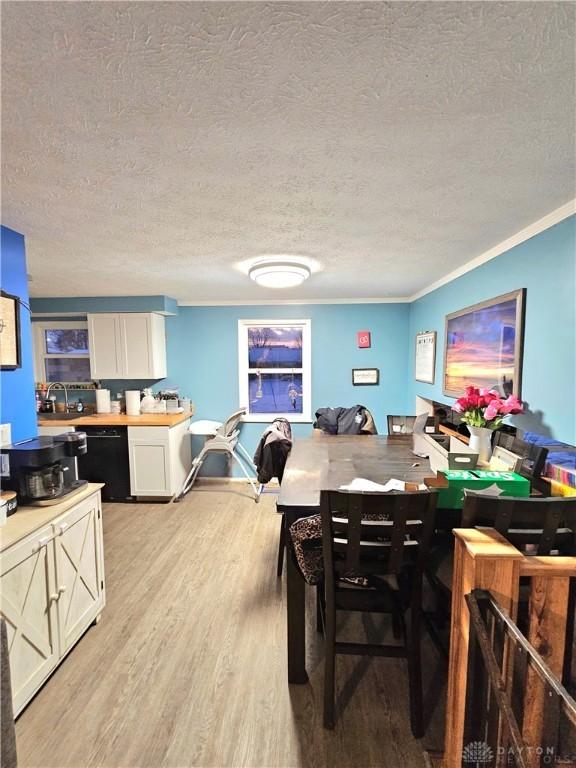 dining area with light wood-type flooring, ornamental molding, and a textured ceiling