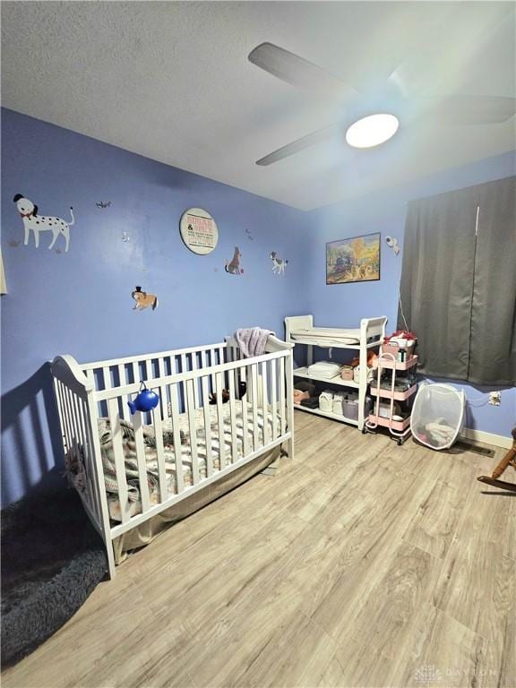 bedroom with hardwood / wood-style flooring, a nursery area, and ceiling fan