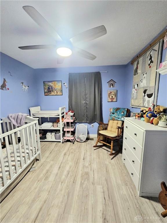 bedroom with ceiling fan, a crib, and light hardwood / wood-style flooring