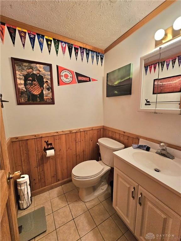 bathroom featuring toilet, vanity, tile patterned floors, wood walls, and a textured ceiling