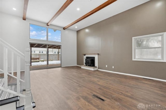 unfurnished living room featuring beam ceiling, a high ceiling, and hardwood / wood-style floors