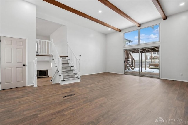 unfurnished living room with a towering ceiling, dark hardwood / wood-style floors, and beamed ceiling