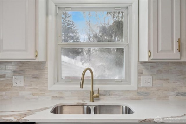 interior details with light stone countertops, sink, white cabinetry, and backsplash