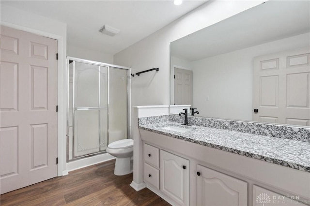 bathroom featuring toilet, vanity, wood-type flooring, and a shower with door