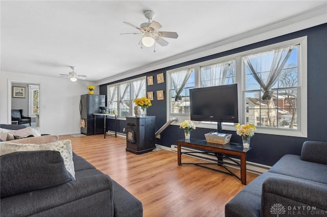 living room featuring ceiling fan, a wood stove, wood-type flooring, and a baseboard radiator