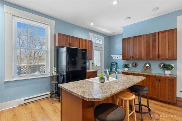 kitchen with a baseboard radiator, black fridge, a center island with sink, and light wood-type flooring