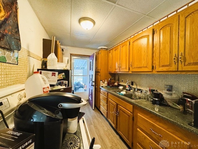 kitchen with decorative backsplash, light wood-type flooring, a paneled ceiling, dark stone countertops, and sink