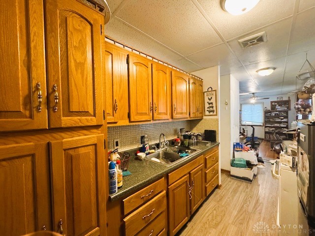 kitchen featuring ceiling fan, tasteful backsplash, light wood-type flooring, a drop ceiling, and sink