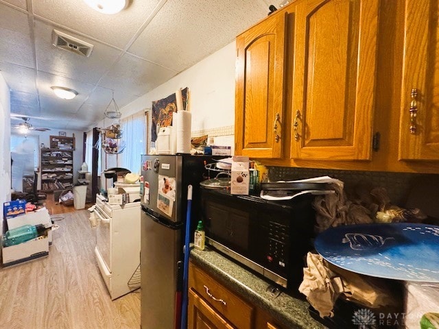 kitchen featuring a paneled ceiling, dark stone countertops, stainless steel fridge, light wood-type flooring, and ceiling fan