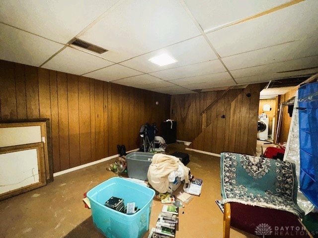 basement featuring a paneled ceiling, wooden walls, and washer / dryer