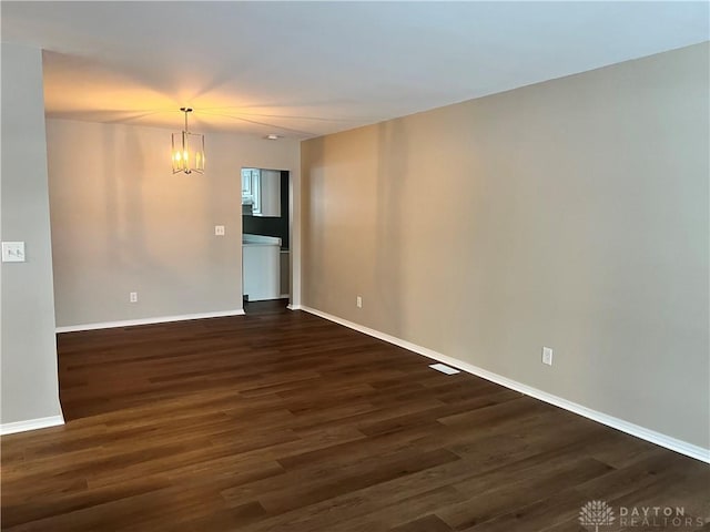 spare room with dark hardwood / wood-style flooring and an inviting chandelier