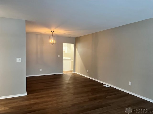 spare room with dark wood-type flooring and a chandelier