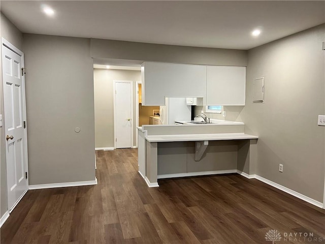 kitchen with a breakfast bar, kitchen peninsula, sink, white cabinetry, and dark wood-type flooring