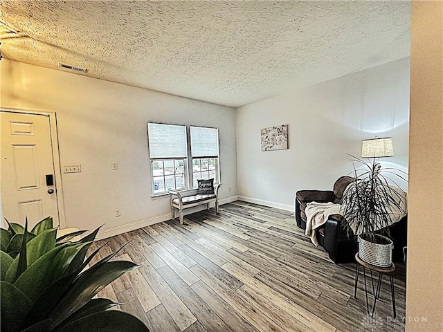 living area featuring a textured ceiling, wood finished floors, visible vents, and baseboards