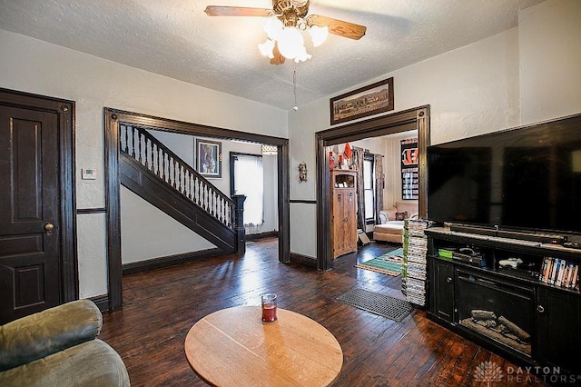 living area featuring a textured ceiling, a ceiling fan, baseboards, stairs, and wood-type flooring