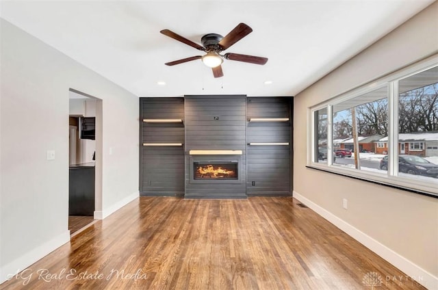 unfurnished living room with ceiling fan, a large fireplace, and hardwood / wood-style floors