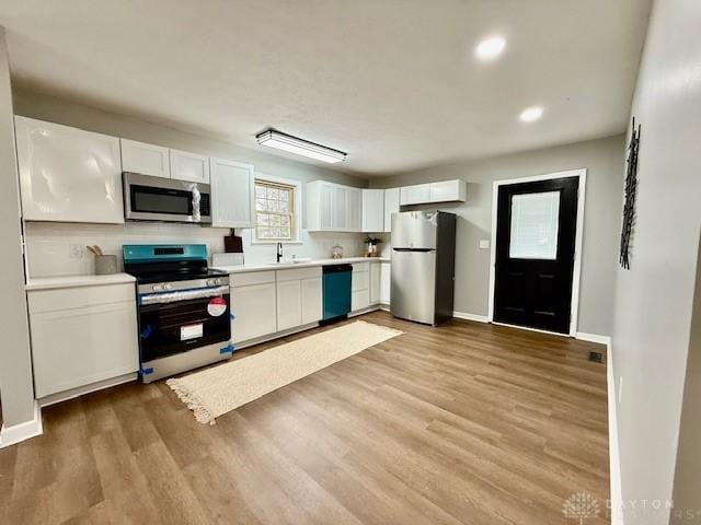 kitchen featuring tasteful backsplash, light hardwood / wood-style floors, sink, white cabinetry, and stainless steel appliances