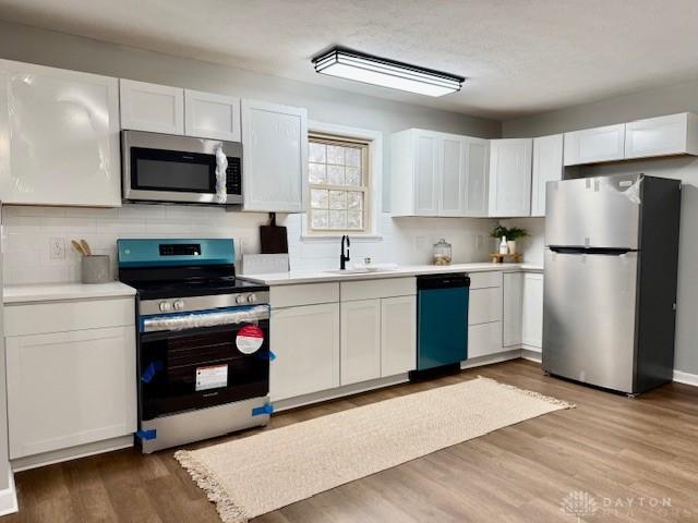 kitchen with stainless steel appliances, light hardwood / wood-style flooring, white cabinetry, and sink