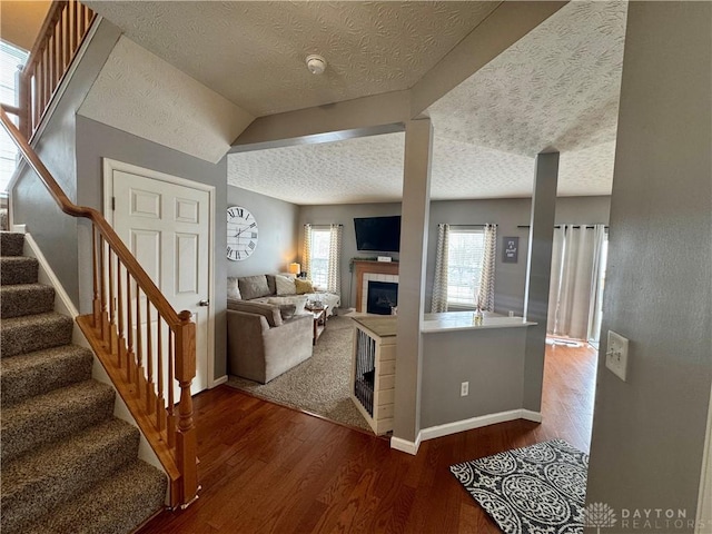 living room with lofted ceiling, wood-type flooring, a tile fireplace, and a textured ceiling