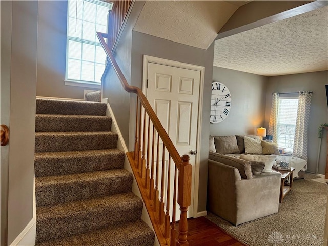 stairway with a textured ceiling, vaulted ceiling, and hardwood / wood-style flooring