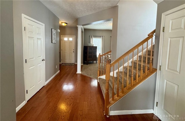 entrance foyer featuring a textured ceiling, ornate columns, and dark hardwood / wood-style flooring