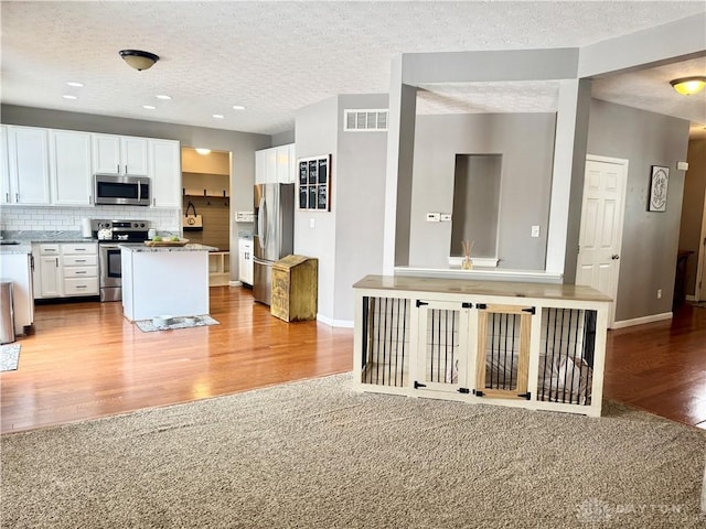 kitchen featuring light carpet, white cabinetry, stainless steel appliances, backsplash, and light stone counters