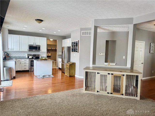 kitchen with white cabinets, appliances with stainless steel finishes, a center island, light carpet, and tasteful backsplash