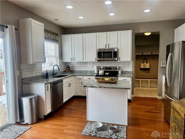 kitchen with appliances with stainless steel finishes, a center island, white cabinetry, sink, and light stone counters