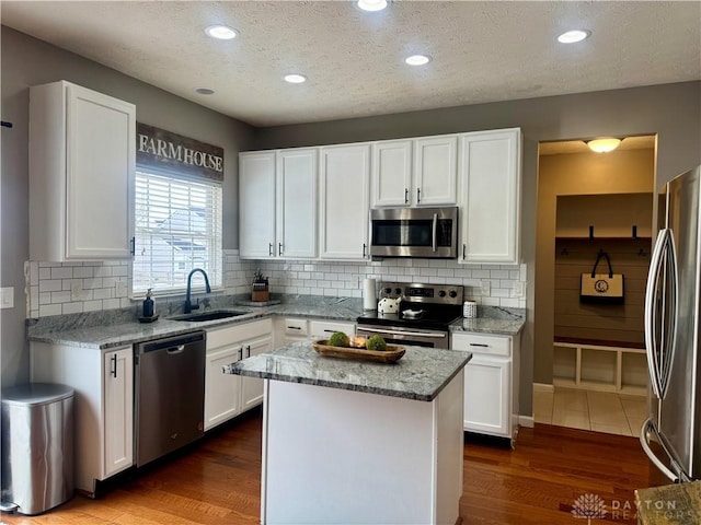 kitchen featuring a kitchen island, sink, white cabinetry, stainless steel appliances, and light stone counters