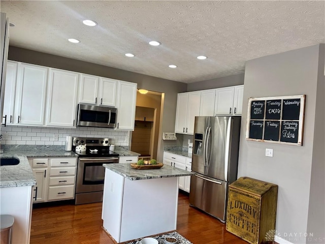 kitchen with light stone countertops, appliances with stainless steel finishes, white cabinetry, and a textured ceiling