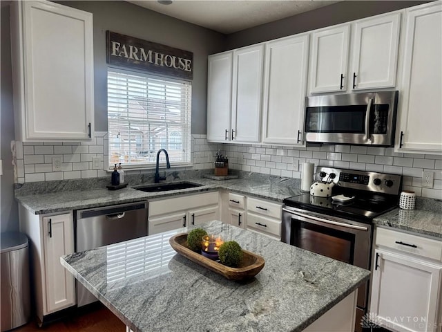 kitchen featuring appliances with stainless steel finishes, white cabinetry, light stone counters, and sink