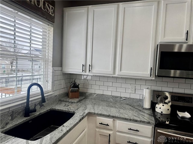 kitchen with light stone countertops, stainless steel appliances, white cabinets, and sink