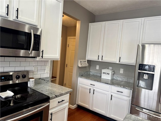 kitchen featuring appliances with stainless steel finishes, white cabinets, tasteful backsplash, and light stone countertops