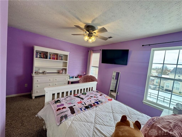 bedroom featuring ceiling fan, dark carpet, multiple windows, and a textured ceiling