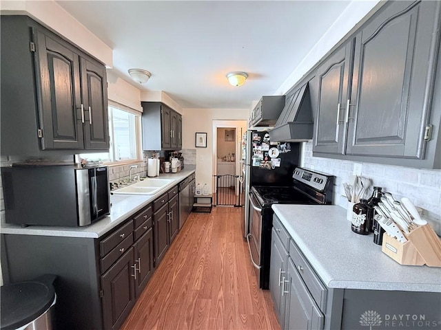 kitchen featuring light countertops, custom range hood, appliances with stainless steel finishes, light wood-style floors, and a sink