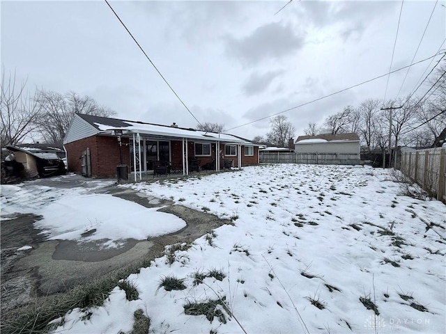 snow covered house with brick siding and fence