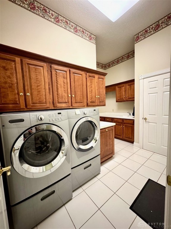 clothes washing area featuring light tile patterned floors, a textured ceiling, cabinets, and washing machine and clothes dryer