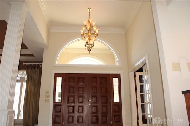 foyer entrance featuring crown molding, decorative columns, and a chandelier