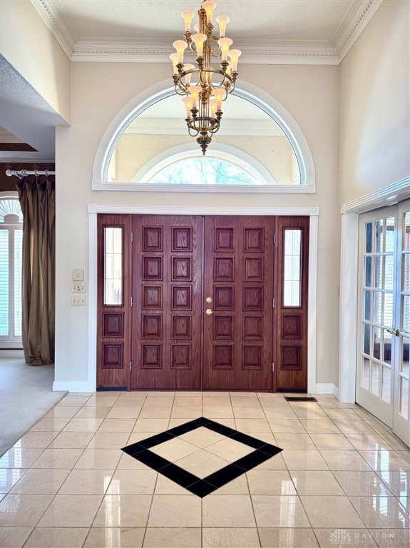 foyer entrance with an inviting chandelier, a towering ceiling, ornamental molding, and french doors