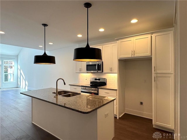 kitchen with white cabinetry, stainless steel appliances, dark stone counters, sink, and a center island with sink