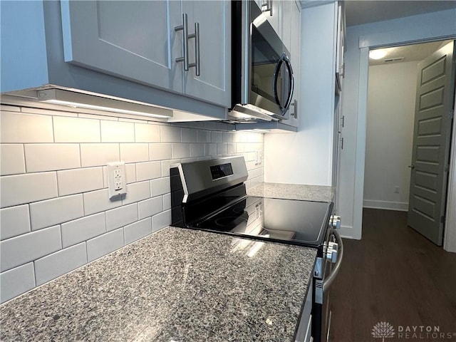 kitchen with dark stone countertops, dark wood-type flooring, appliances with stainless steel finishes, and tasteful backsplash