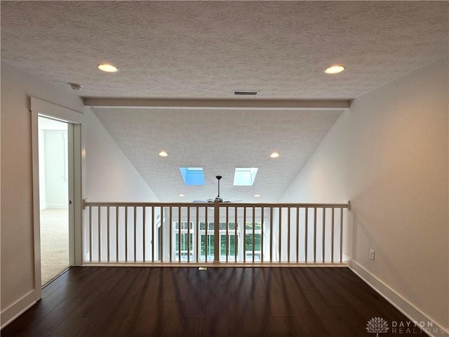 unfurnished room with ceiling fan, vaulted ceiling with skylight, dark hardwood / wood-style flooring, and a textured ceiling