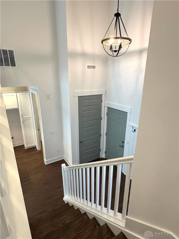 stairs with wood-type flooring, a towering ceiling, and an inviting chandelier